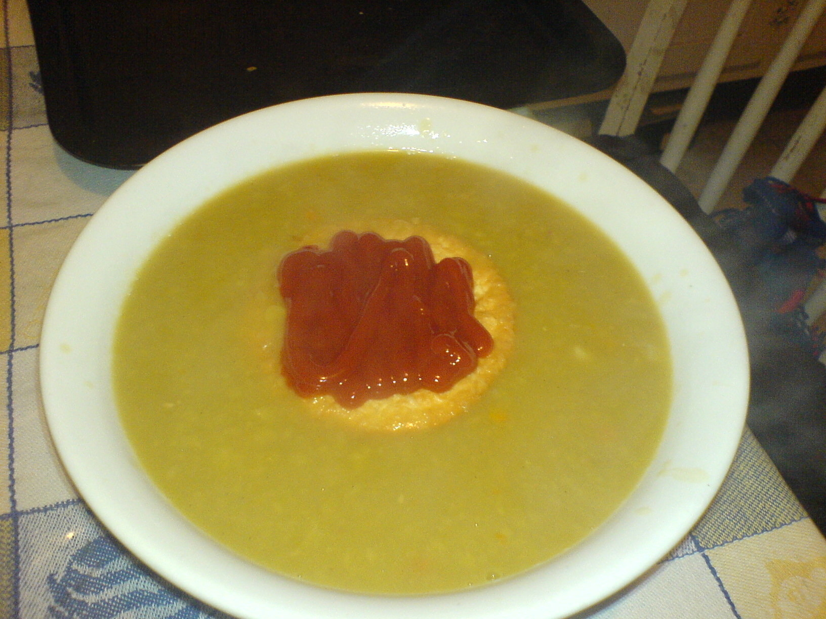 A plate filled with pea soup with a submerged meat pie with tomato sauce on top