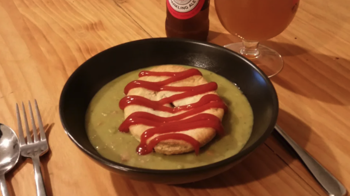 A plate filled with pea soup with a meat pie with tomato sauce on top