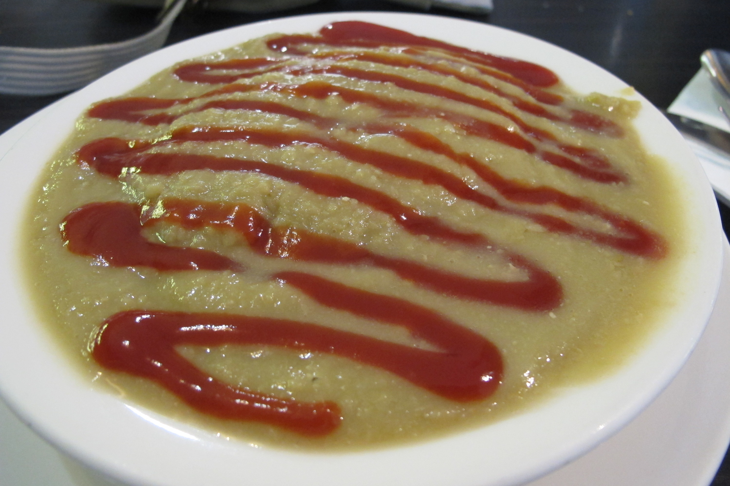 A plate filled with a runny pea soup that has tomato sauce on top