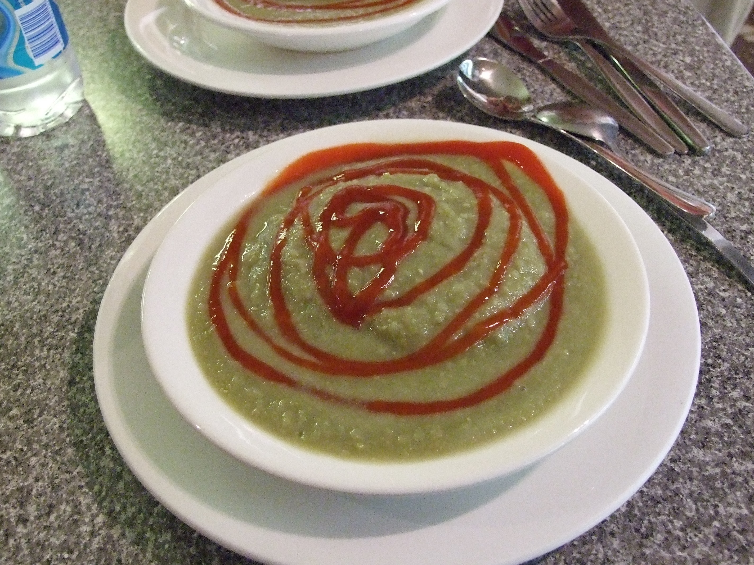 A plate filled with pea soup with a submerged meat pie with tomato sauce on top