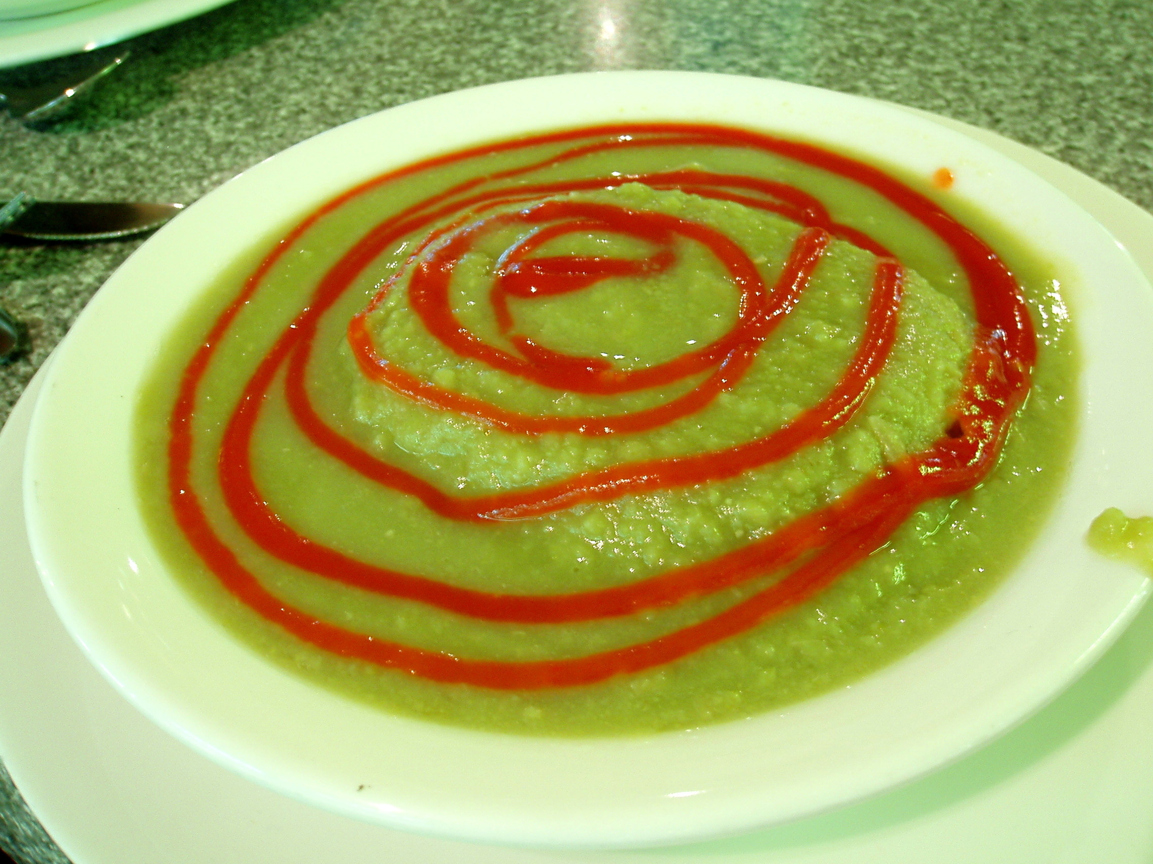 A plate filled with pea soup with a submerged meat pie with tomato sauce on top