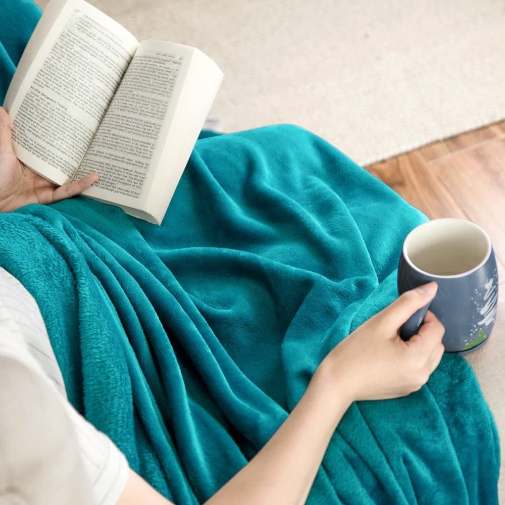 Model wearing the teal blanket while reading and holding a mug