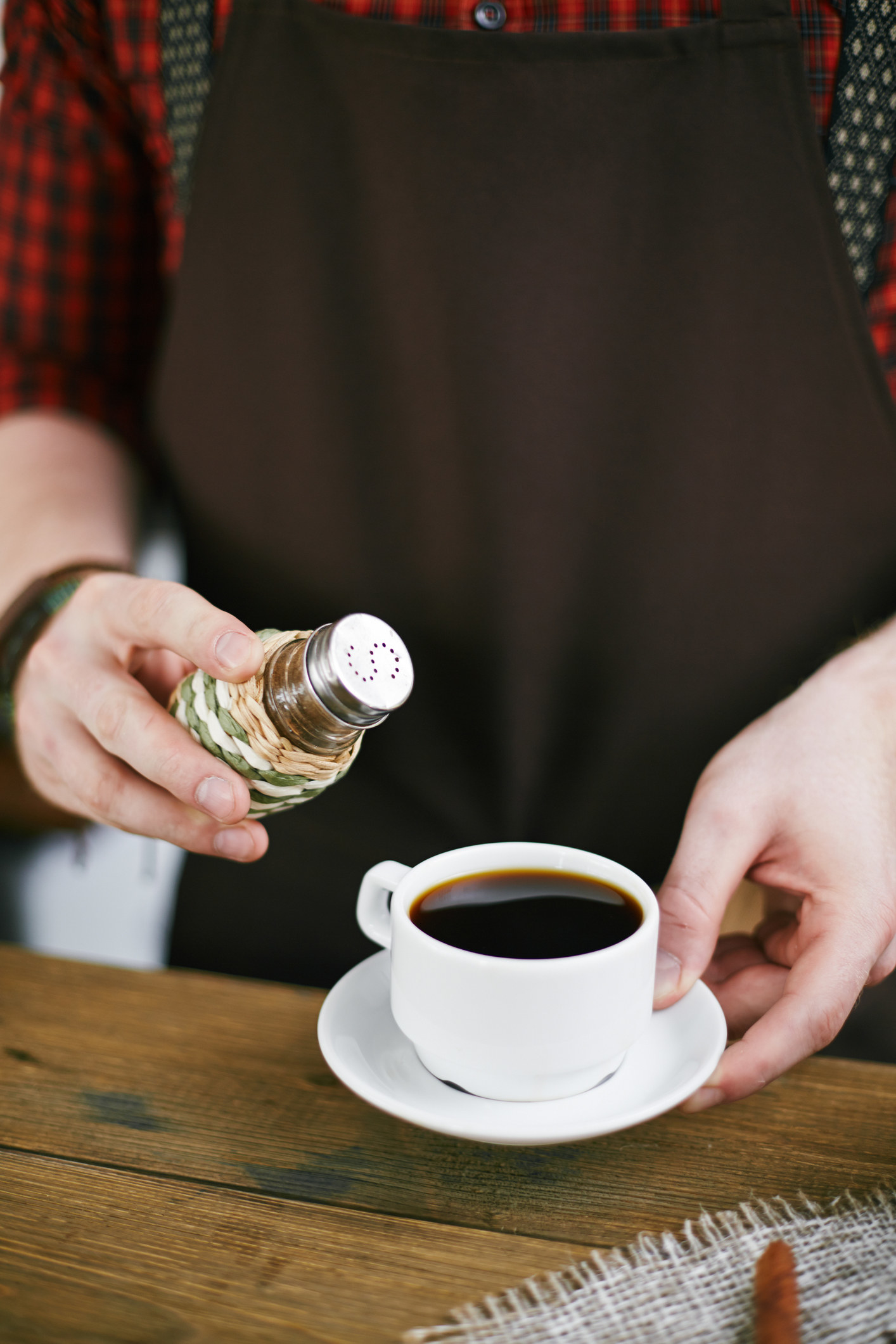 Hands of barista adding salt in black coffee