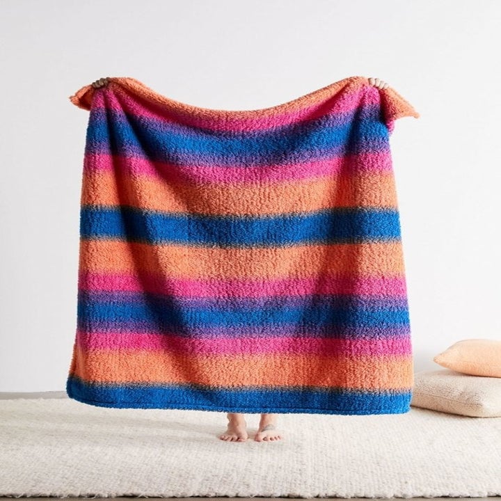Person holding up blue, pink, and orange blanket