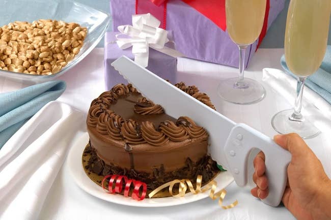 A hand using the knife to cut through a chocolate cake