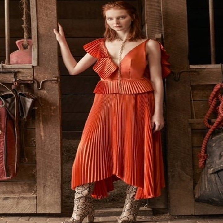 A model in an asymmetric pleated orange midi dress