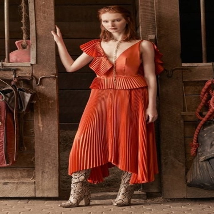 A model in an asymmetric pleated orange midi dress