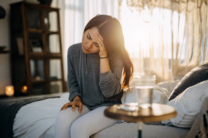 Woman sitting on bed holding her head. 