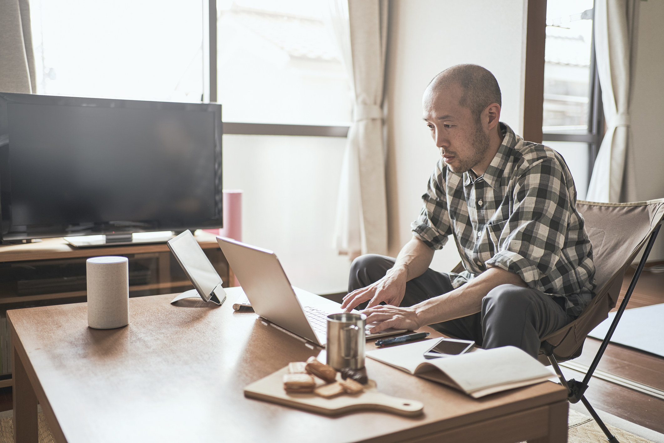 Man sitting at table using laptop with coffee and biscuits nearby. 