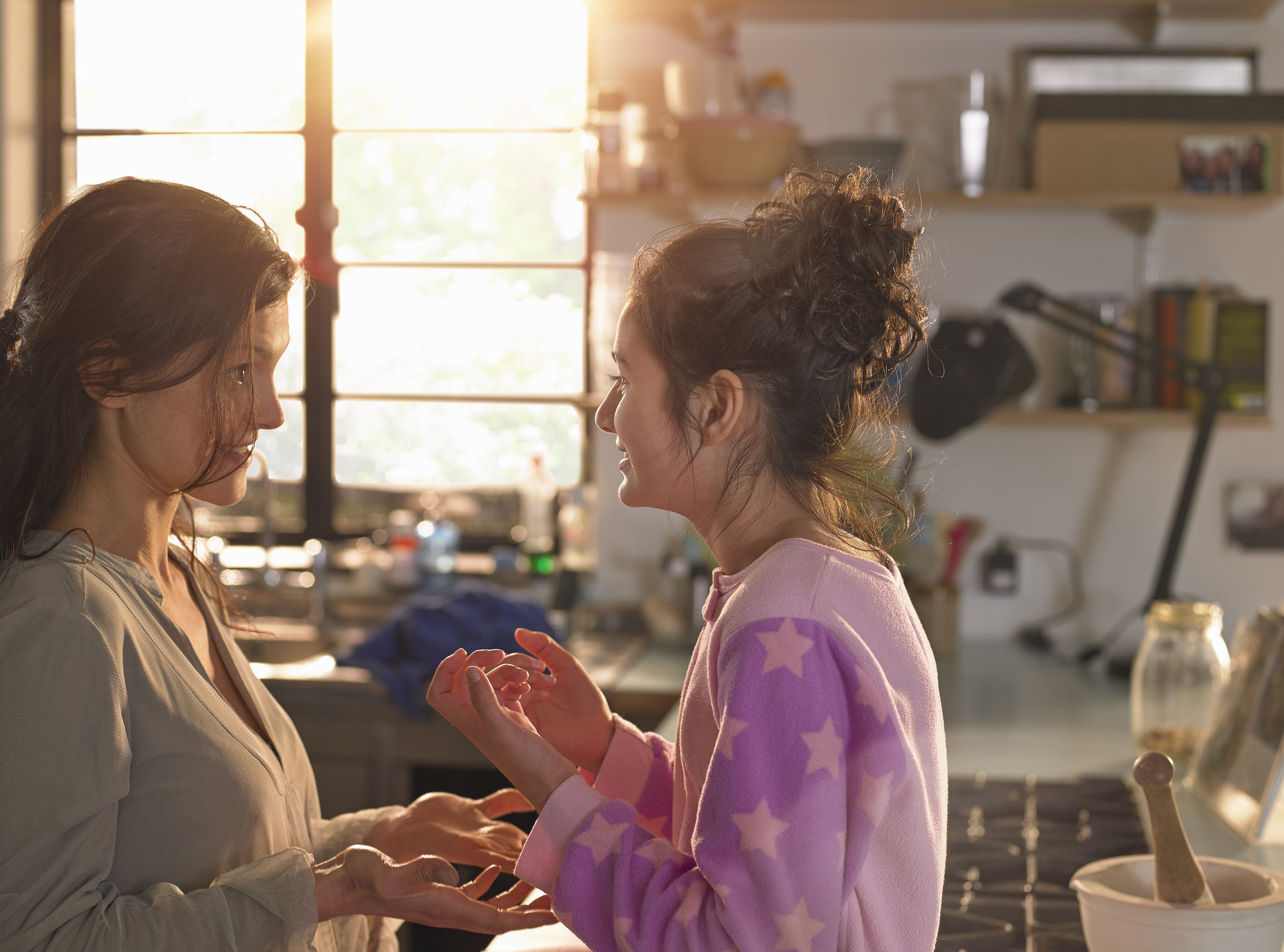 Mother and daughter in the kitchen chatting happily on a sunny morning.