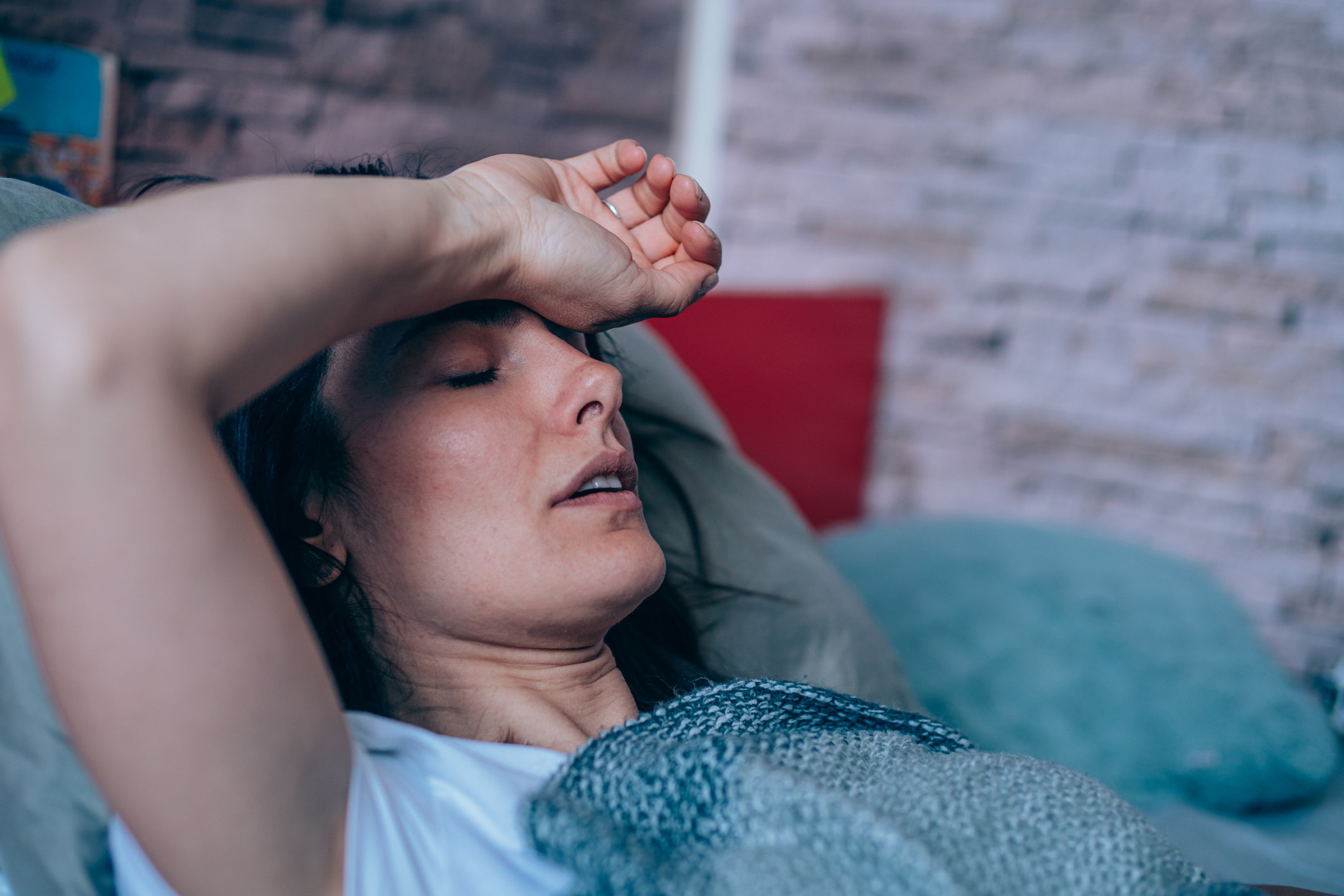 Sick young woman lying in the bed covered with blanket. Ill woman lying in bed with high temperature.