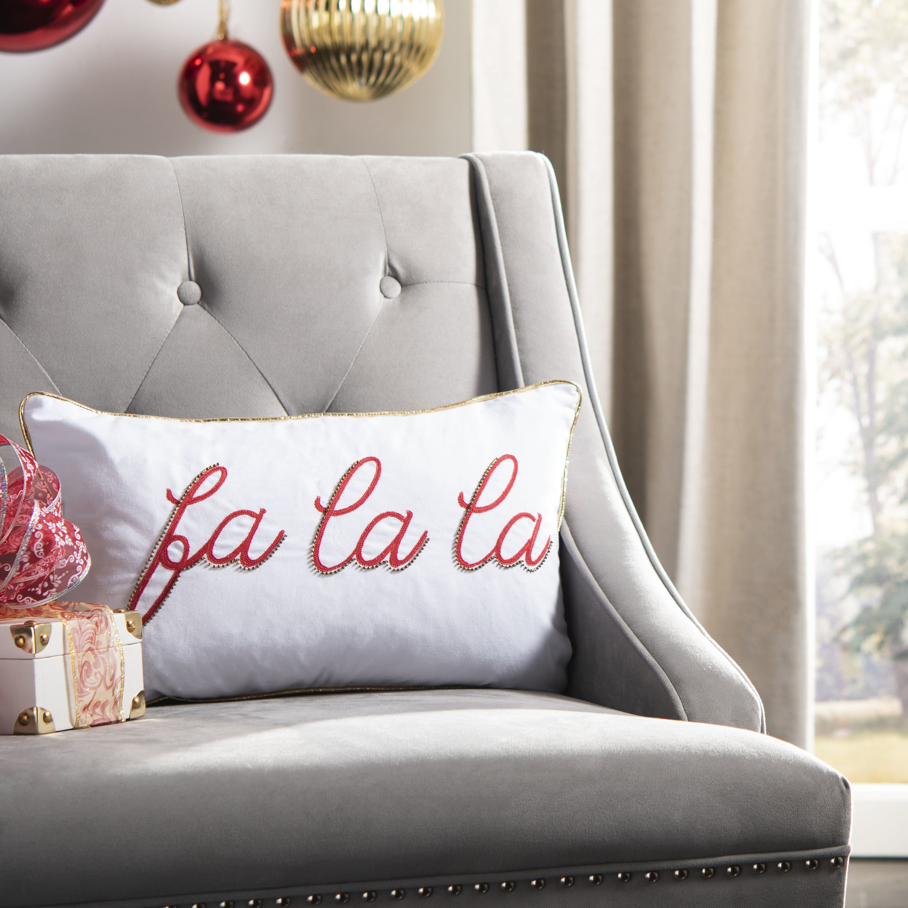a white throw pillow with gold edges and fa la la embroidered in red
