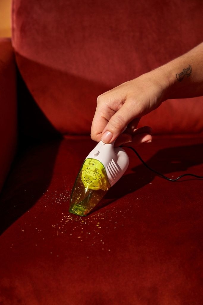 A hand using the green corded vacuum to suck up crumbs on a couch