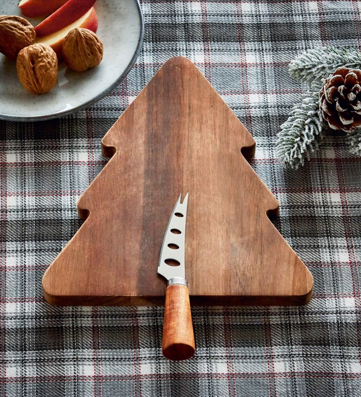 The Christmas tree-shaped cutting board with a cheese knife with wood handle sitting on it