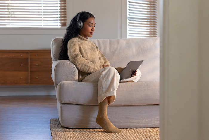 Une personne avec des écouteurs, utilisant le Surface Laptop 3, est assise sur un divan