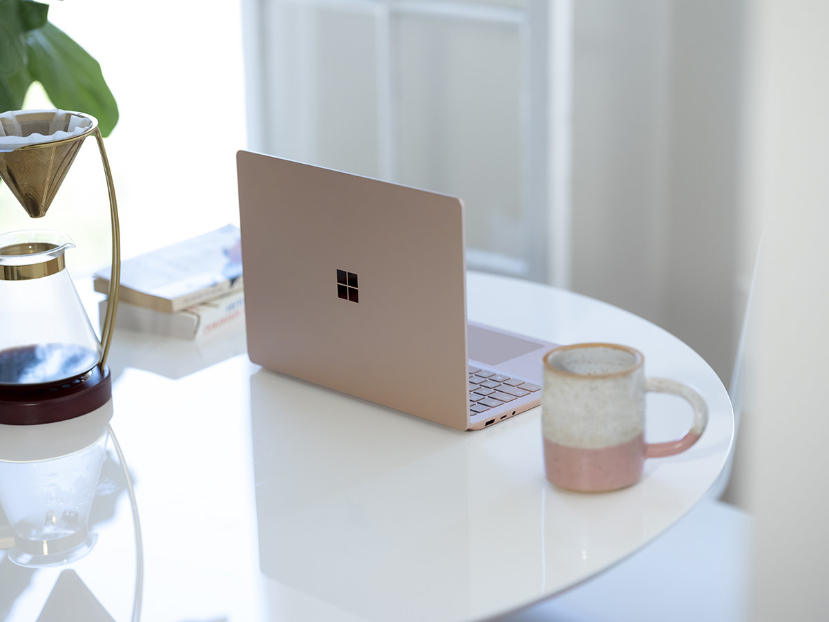 A laptop beside a coffee mug, books, and coffee dripper