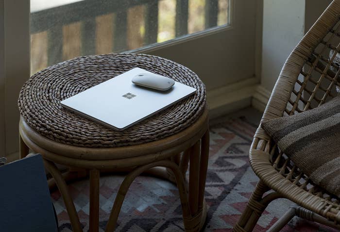 Un ordinateur portable sur une table en rotin à côté d’une chaise assortie