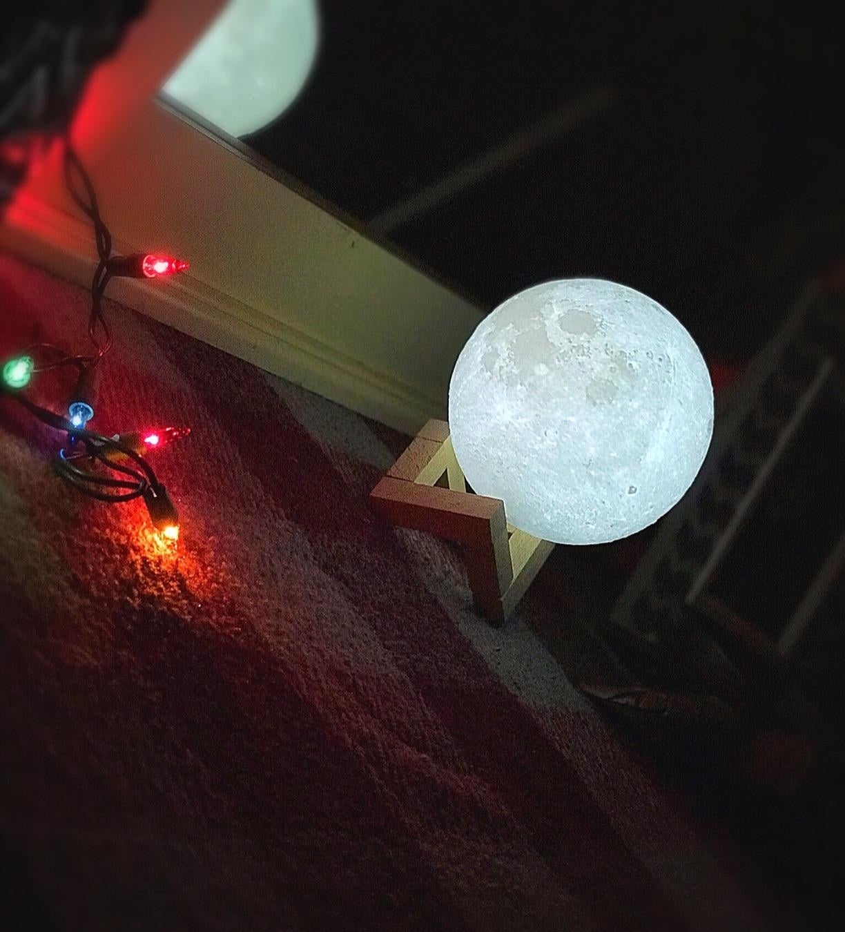 reviewer image of the moon lamp on the floor besides colorful twinkle lights