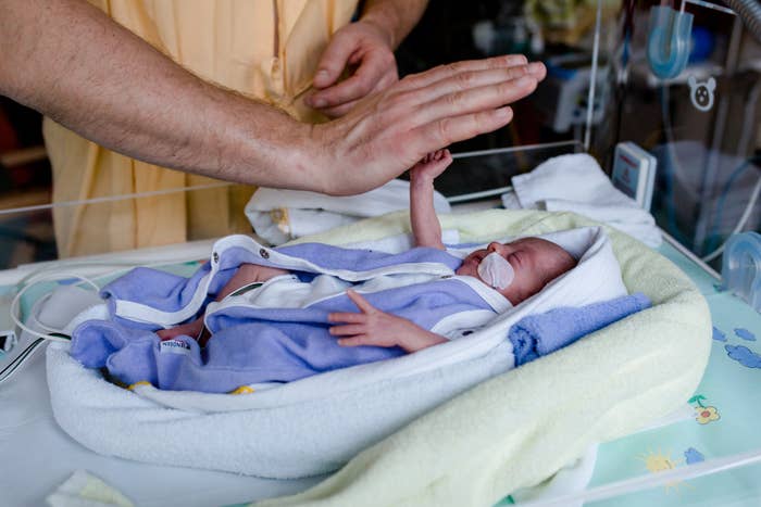 Premature baby lies in the heat bed and gives high five to his Dad.