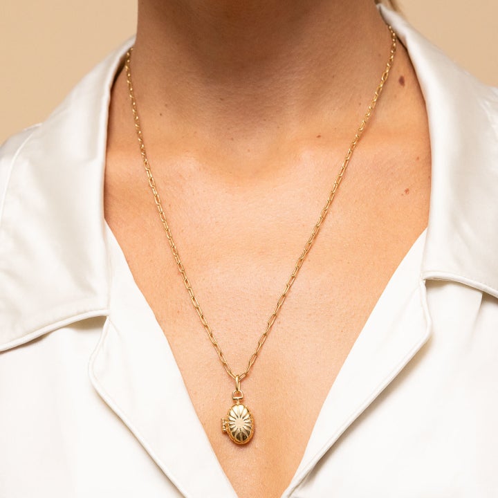 A model wearing a collared V-neck shirt and a gold locket on a slim chain