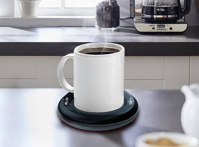 A mug of coffee on top of a black round heated small plate 