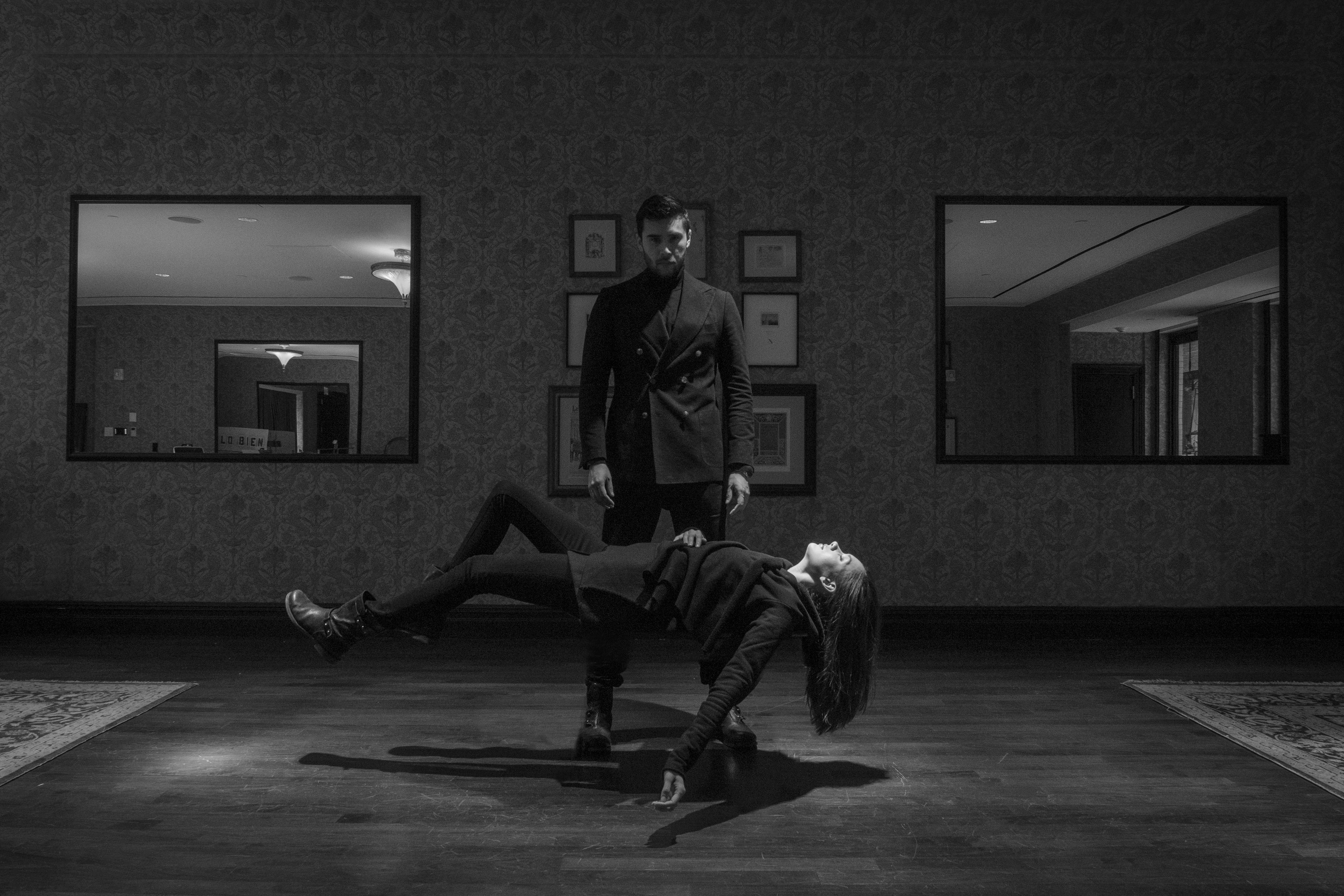 A black-and-white photograph of a man standing in front of a woman levitating