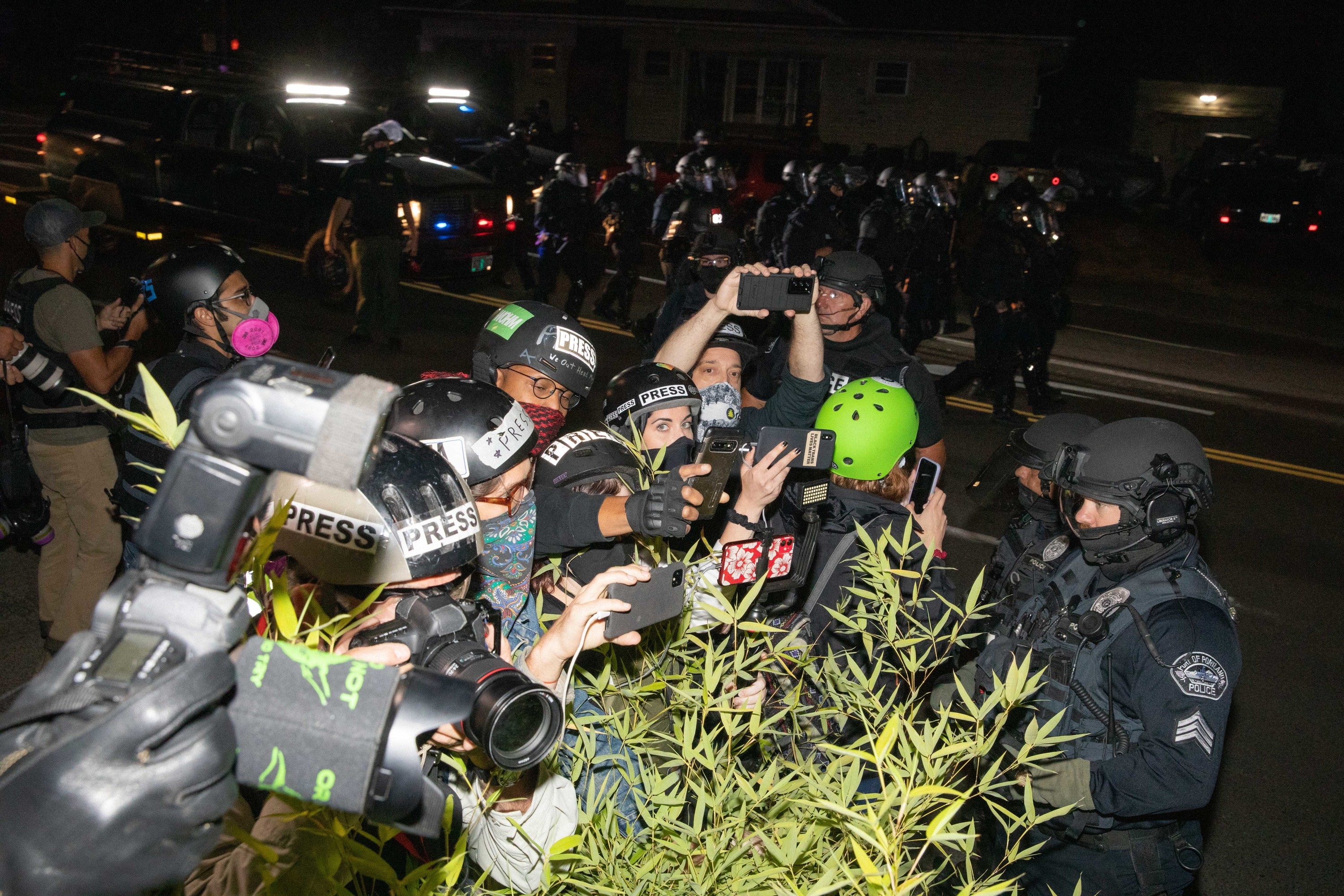 People in press helmets and protest gear crowding around to take photographs in front of police