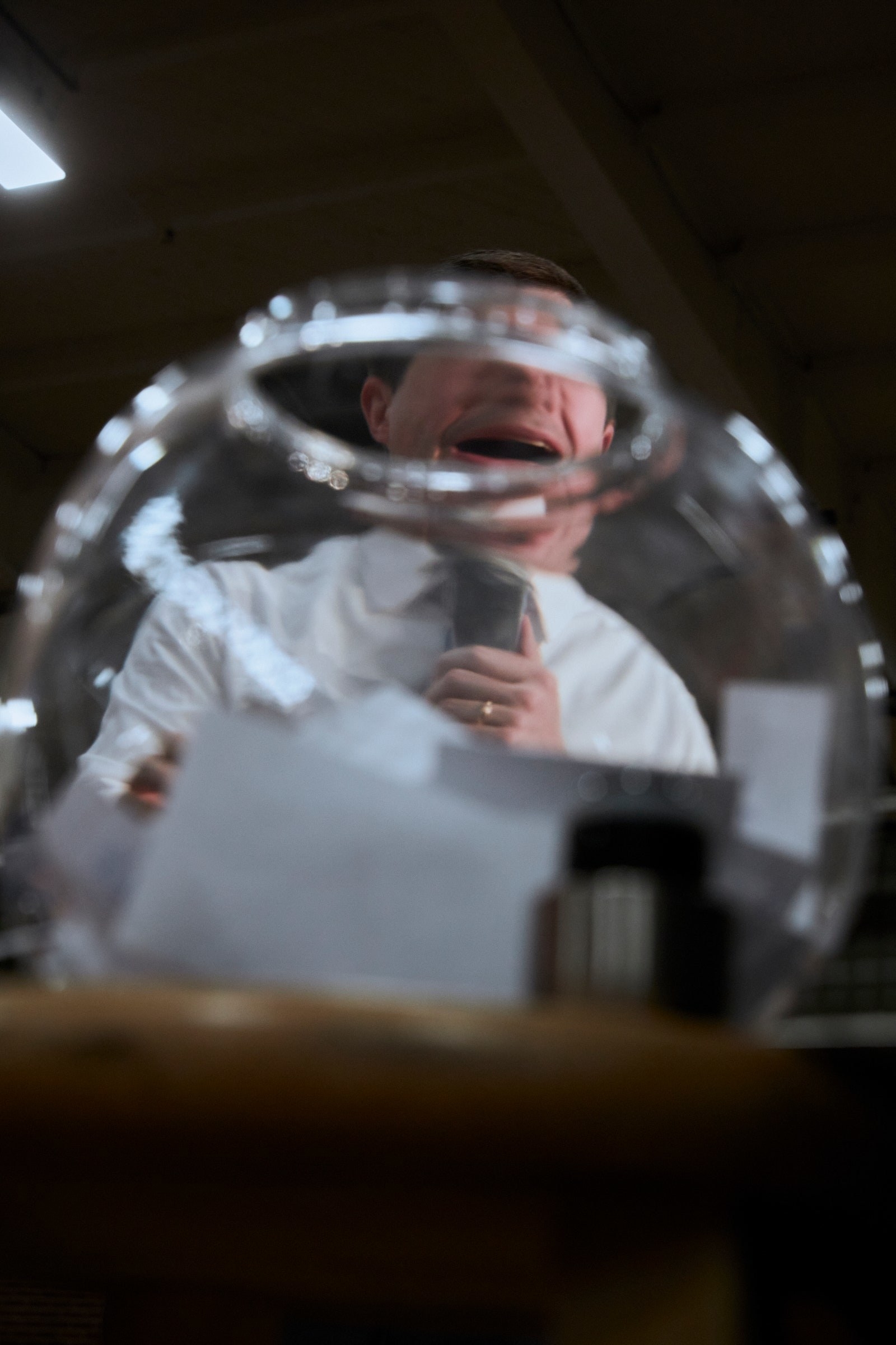 A man speaking into a microphone distorted by a bowl in between him and the camera