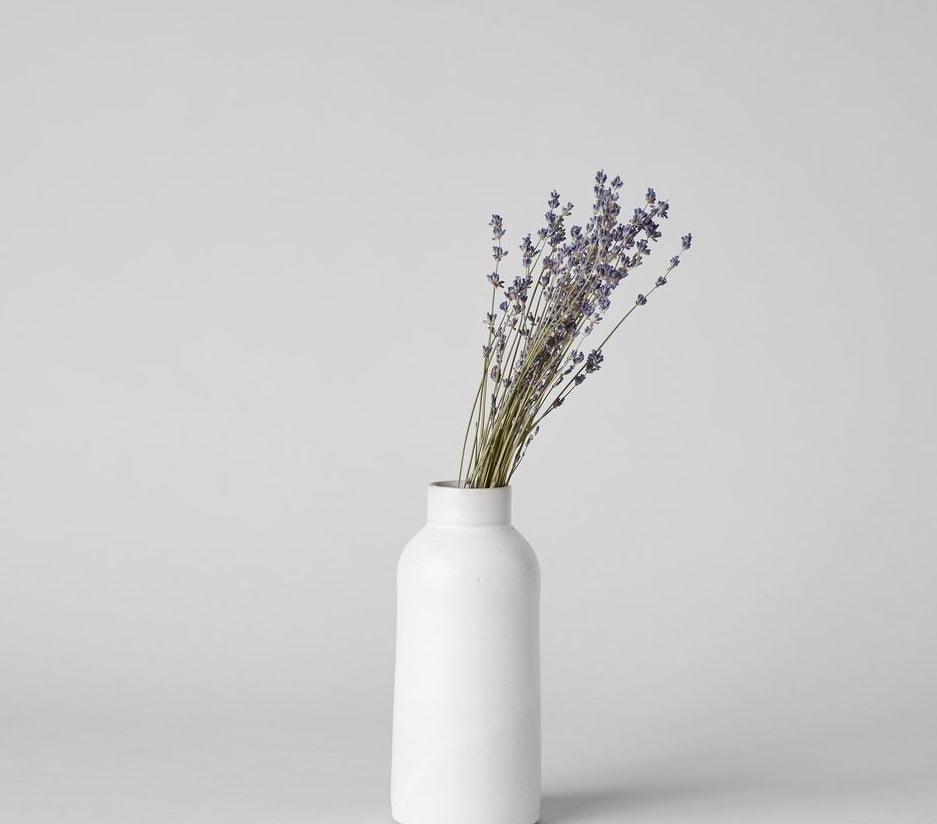 A tall white bottle vase with a bundle of purple flowers in it