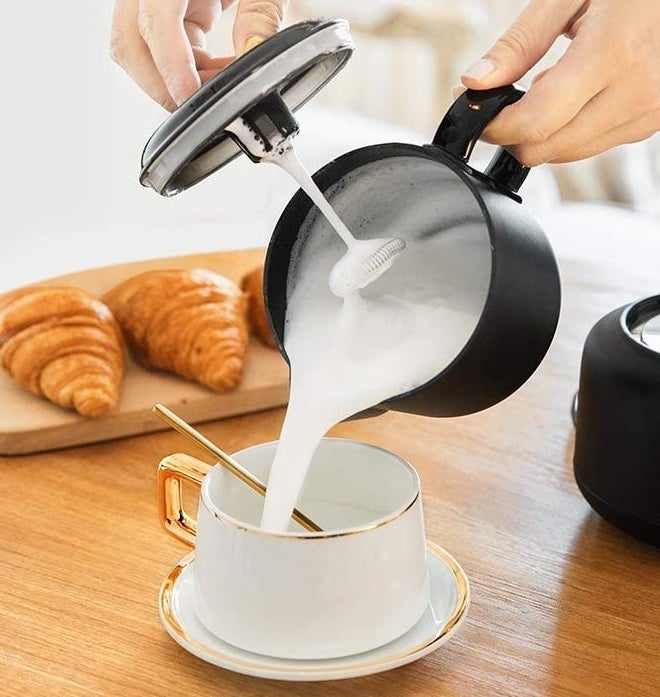 A person pouring frothed milk out of the pot