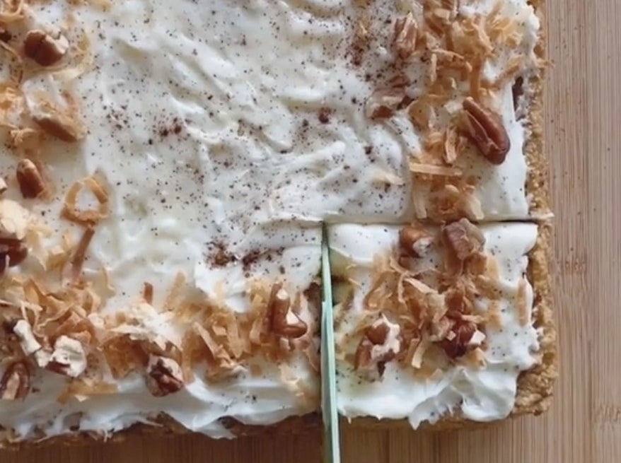 A square cake with white frosting and toasted coconut on top