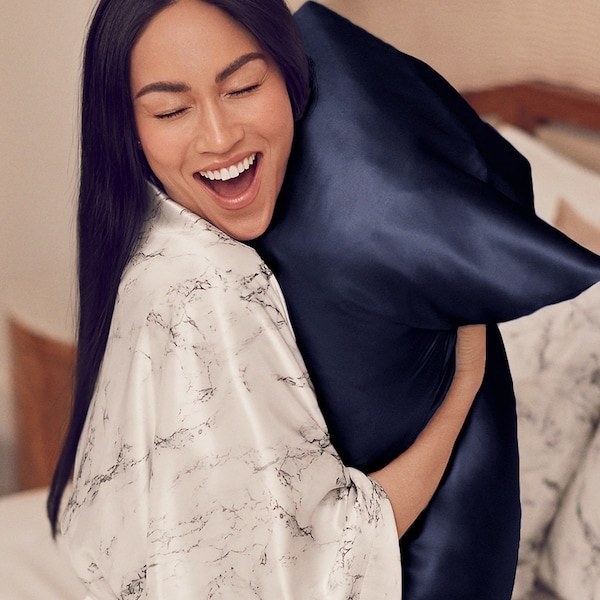 Model hugging a pillow with a navy Slip silk pillowcase on it