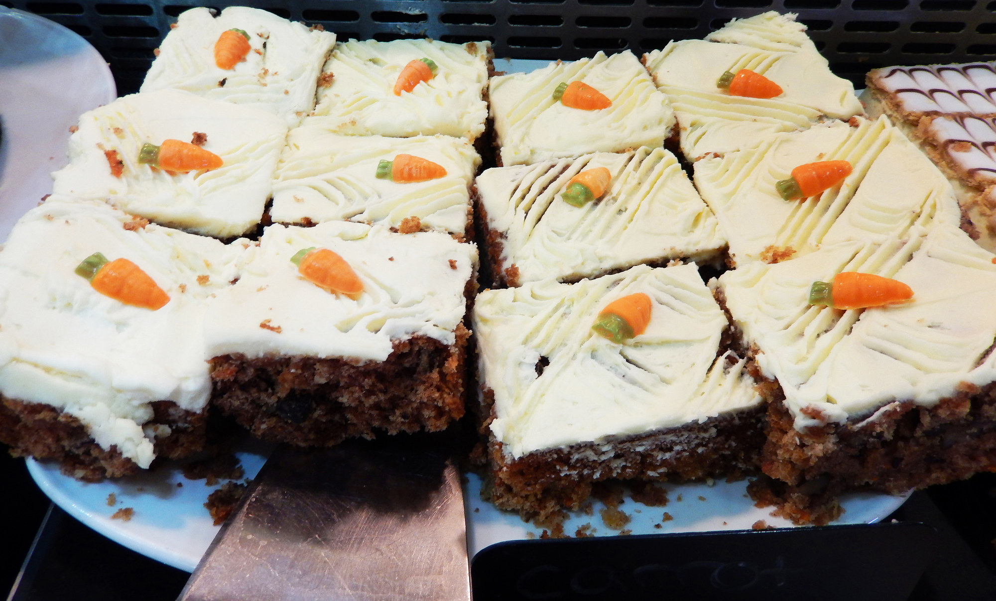 Photo showing an indulgent dessert served at a restaurant - slices of homemade carrot cake.  The carrot cake was topped with a rich cream cheese icing and decorated with orange fondant carrots.