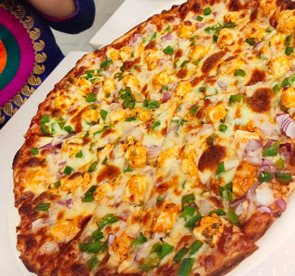A massive pizza with paneer chunks, capsicum and onions
