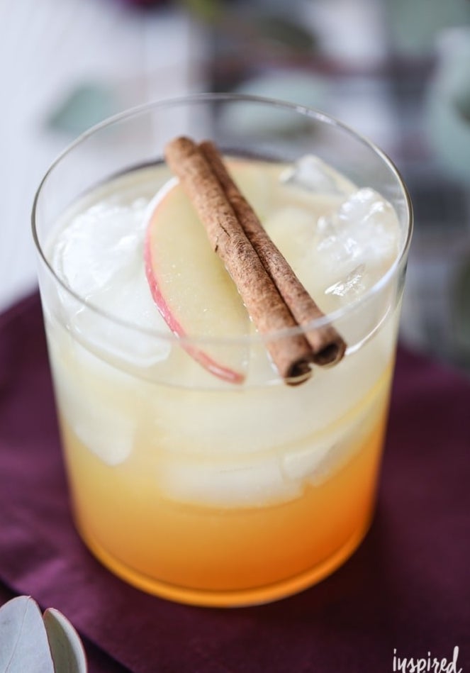 An Apple harvest cocktail topped with sliced apples and cinnamon sticks.
