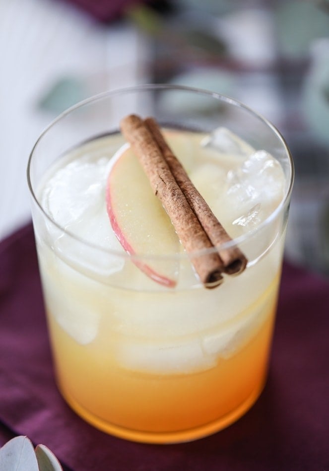 An Apple harvest cocktail topped with sliced apples and cinnamon sticks.
