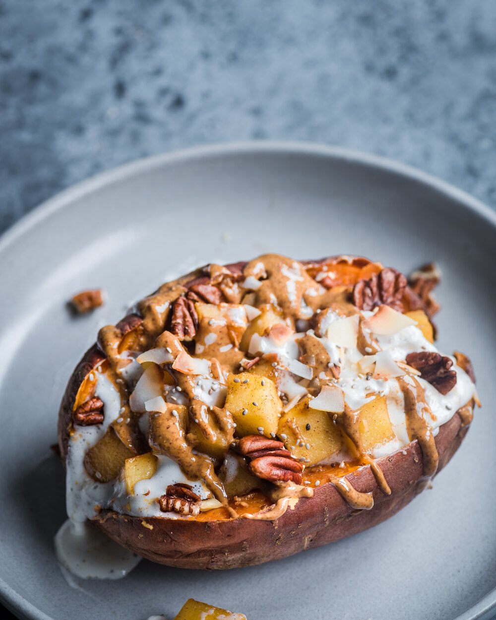 A sweet potato filled with apples, coconut flakes, almond butter, and nuts.