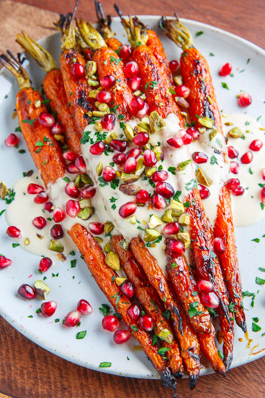A plate of roasted carrots topped with pomegranate seeds, pistachios, and tahini drizzle.