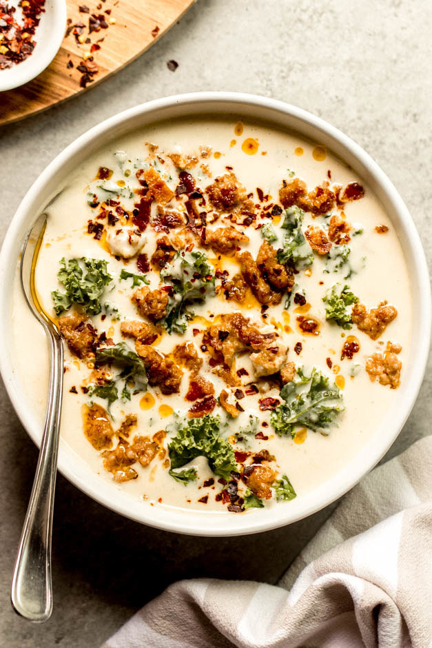 A bowl of cauliflower soup topped with sausage, kale, and red pepper flakes.