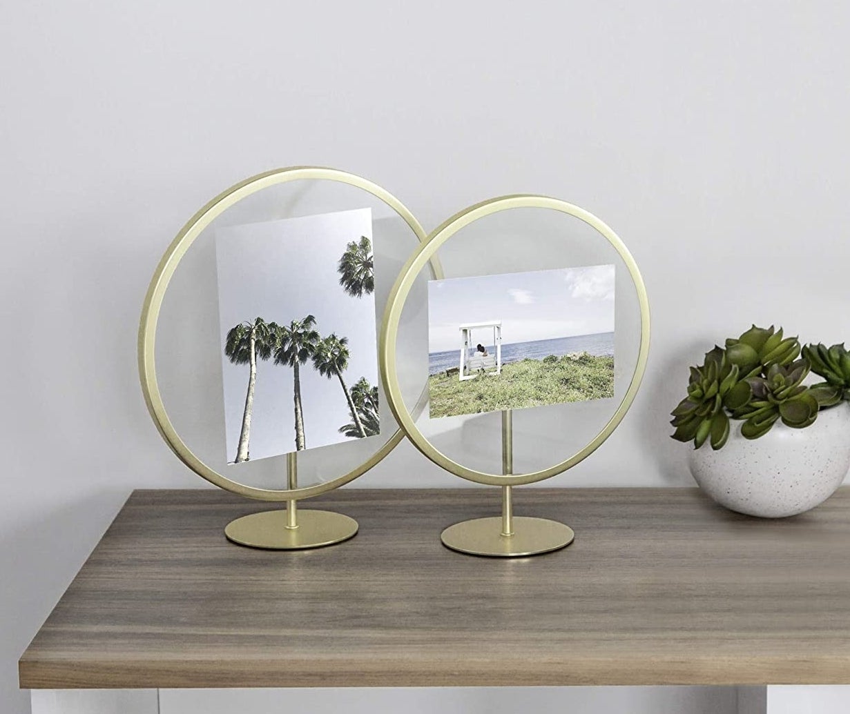 Two gold circular frames and stands with pictures in the glass center