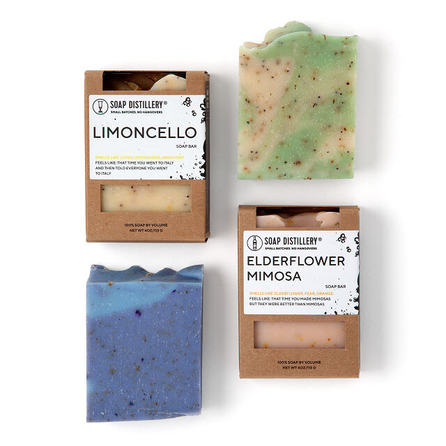 The four soap bars in different colors, two have cardboard packaging on them with labels of Limoncello and Elderflower Mimosa