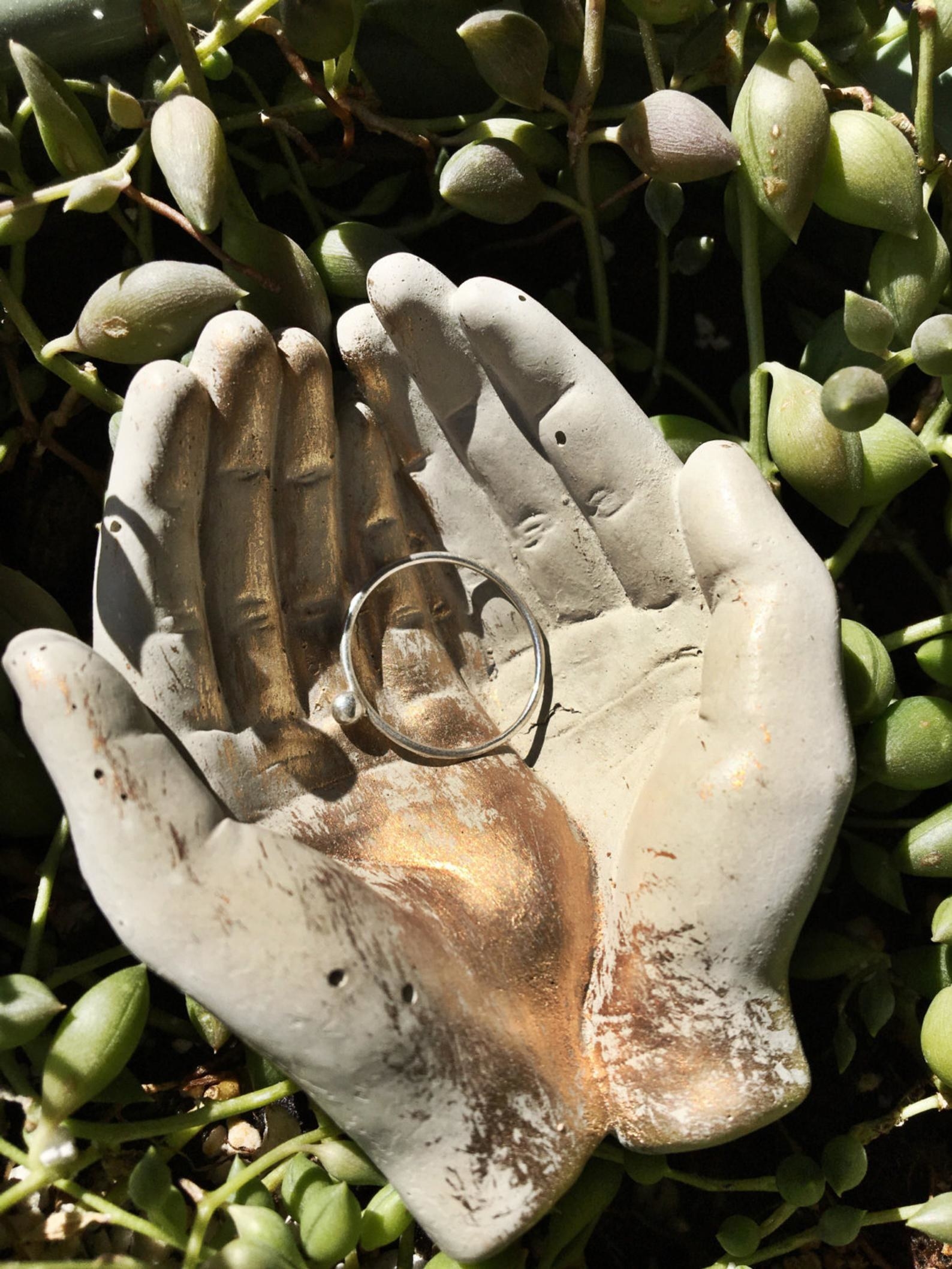 Small beige dish that looks like two hands coming together and holding a ring with gold painted on top