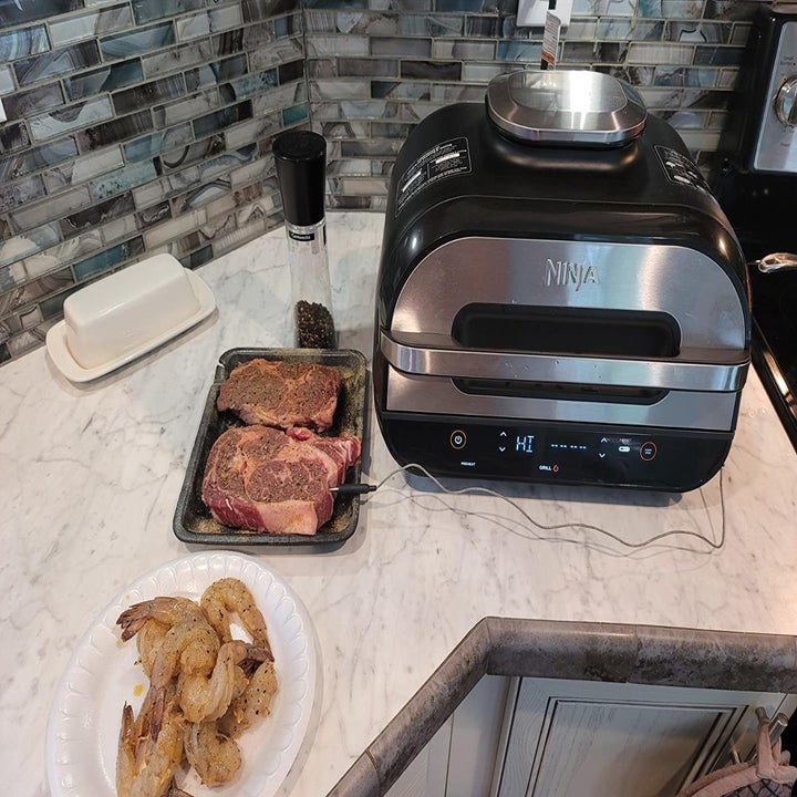 An indoor grill next to raw steak and shrimp being prepped on a kitchen counter
