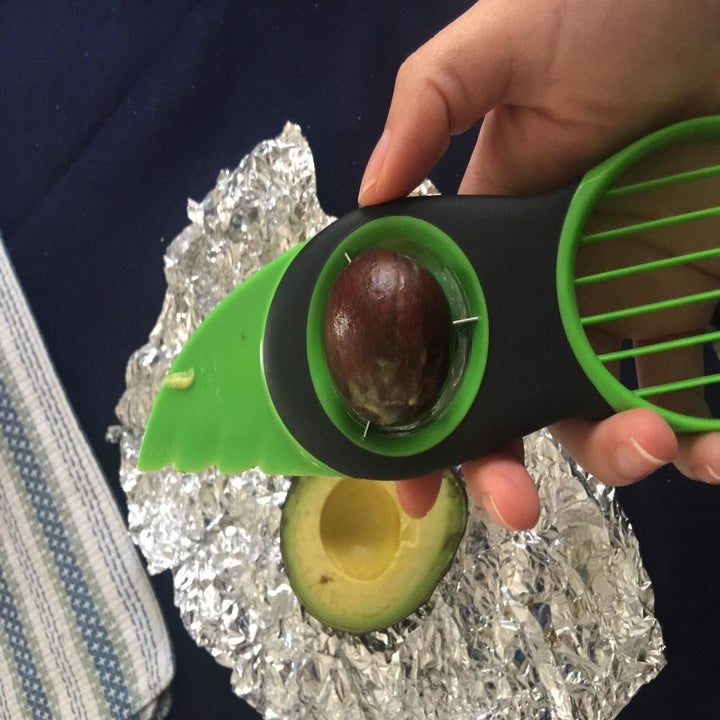 Reviewer holds green avocado slicer that extracted pit from avocado they were about to slice up