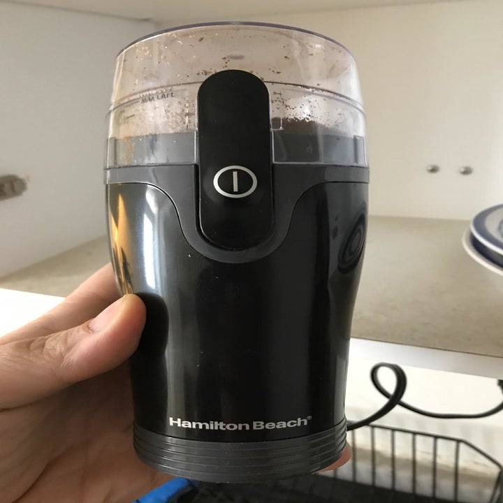 A reviewer holding up an electric spice and coffee grinder