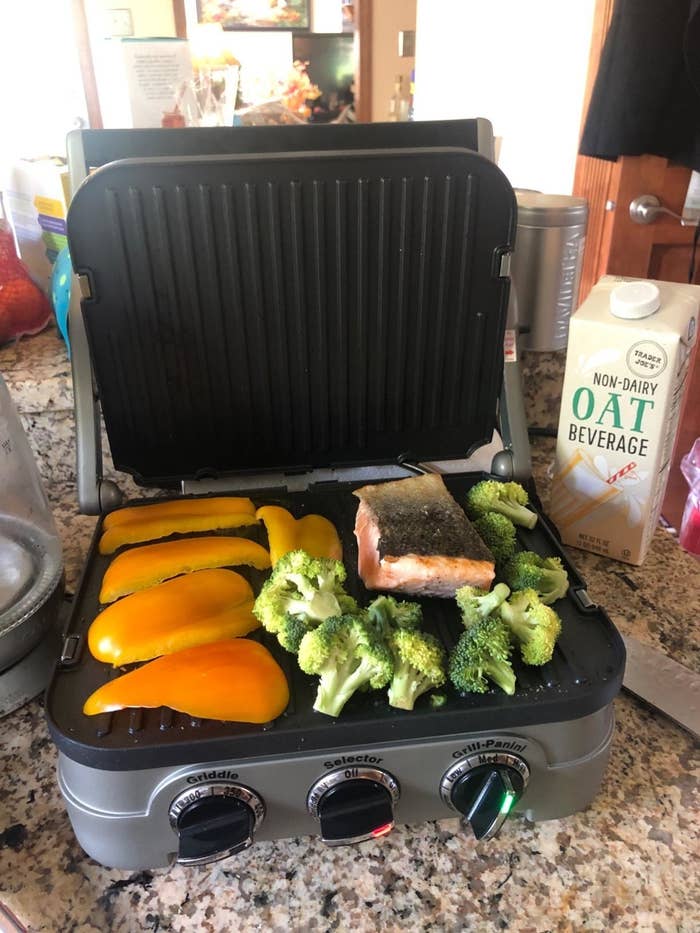 Gray and black 5-in-1 countertop cooker with fresh orange pepper slices, broccoli florets, and a slab of salmon 