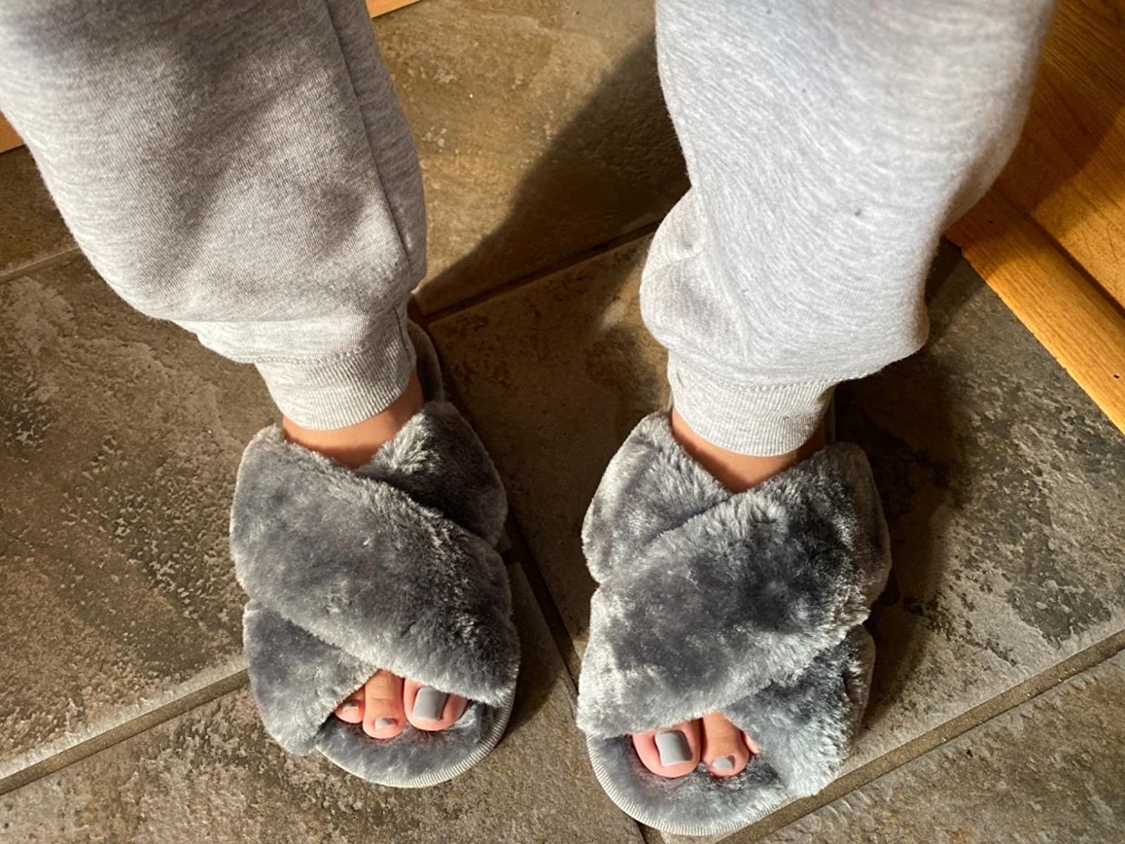 Reviewer wearing the criss-cross open-toe fuzzy slippers in grey