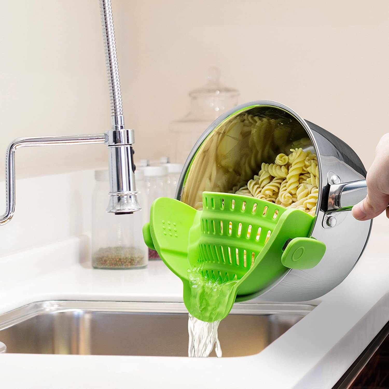 Model uses silver pot with clip-on green strainer to strain water out of a batch of pasta in a sink