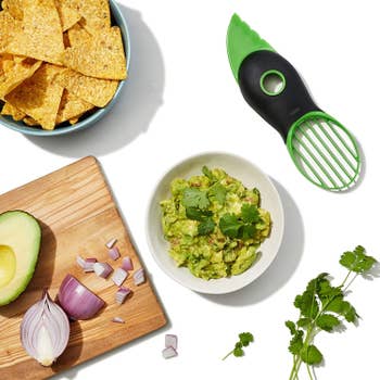 Green avocado slicer next to bowl of guacamole and sliced avocado on a cutting board