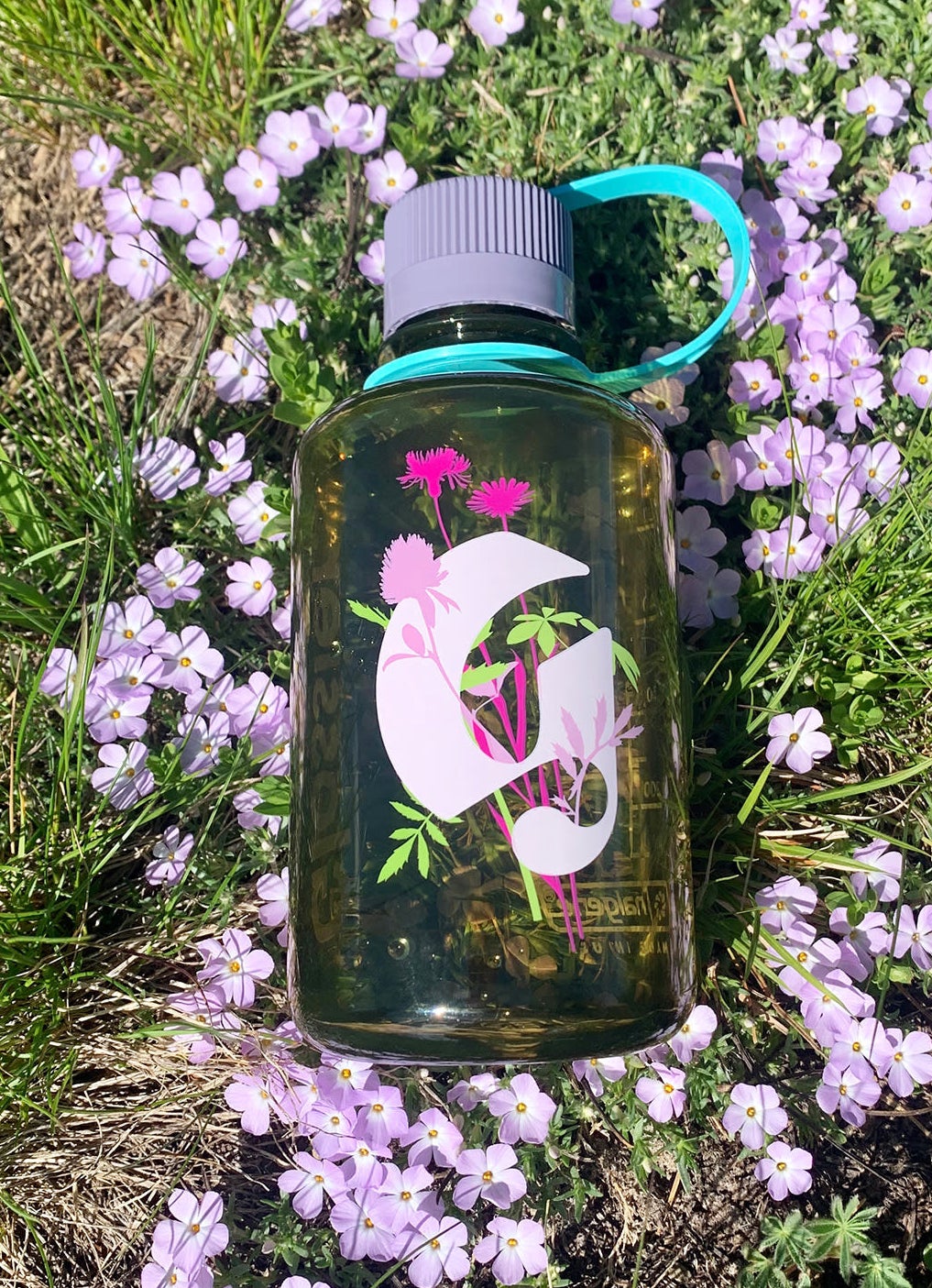 The semi-clear green water bottle with a floral Glossier g logo in pink with flowers on it on the front and grey lid with teal strap